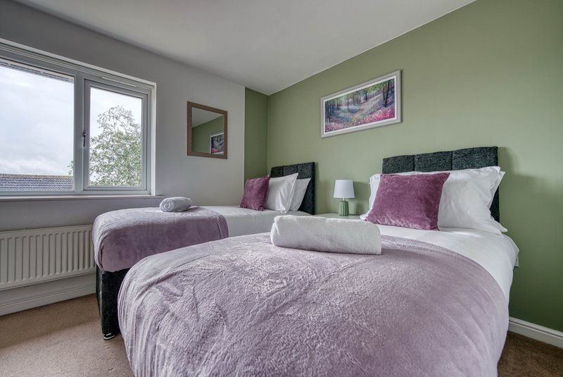 Bedroom with two beds, green walls, window, bedside lamp and framed wall art