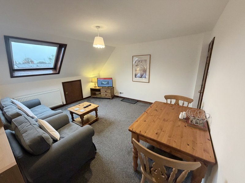 Open-plan living and dining area with grey sofa, wooden table, and skylight window