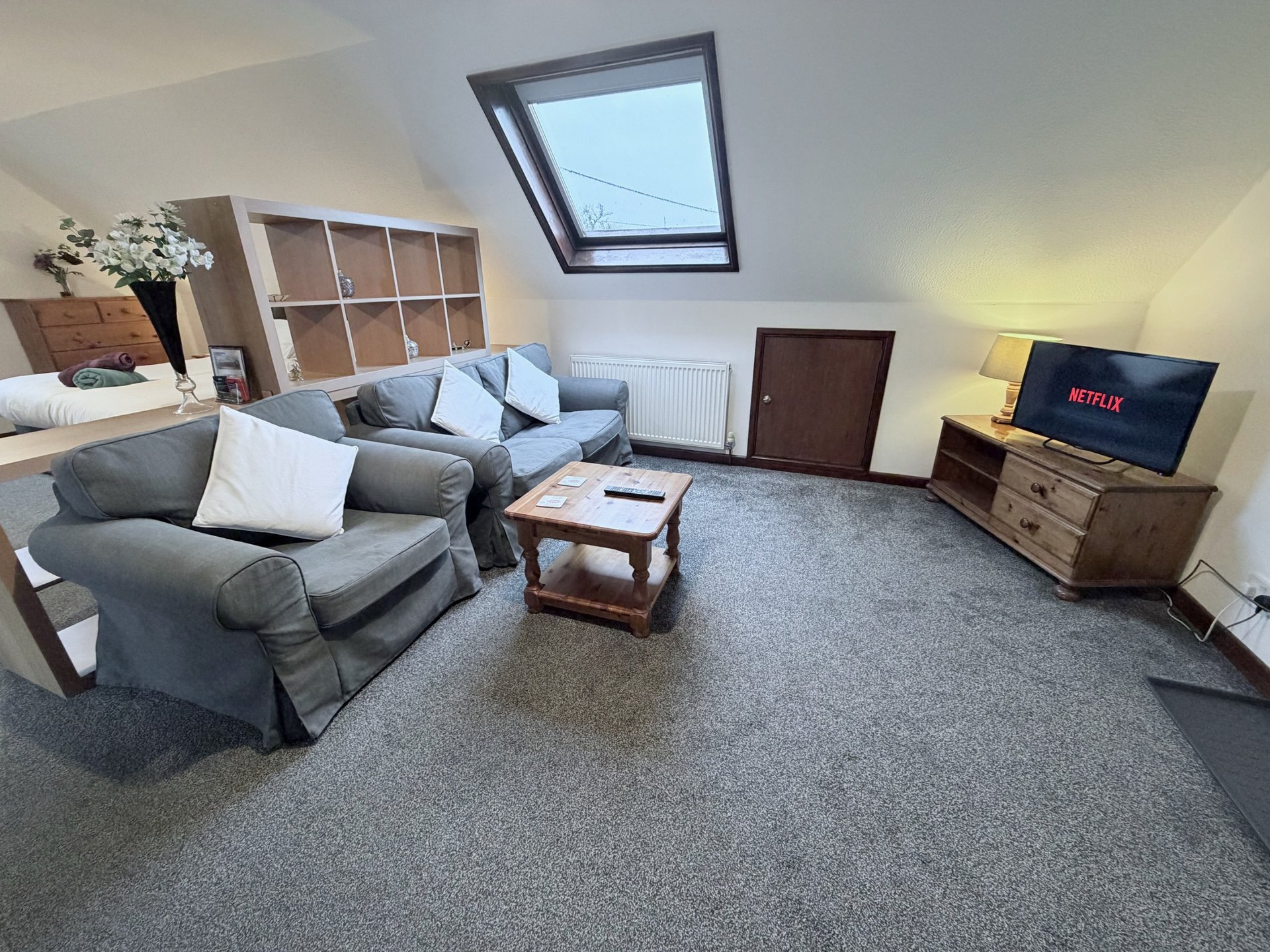 Attic living room with gray sofa, coffee table, TV, and skylight window