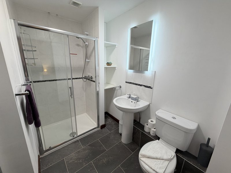 Modern bathroom with glass shower enclosure, pedestal sink, toilet and illuminated mirror