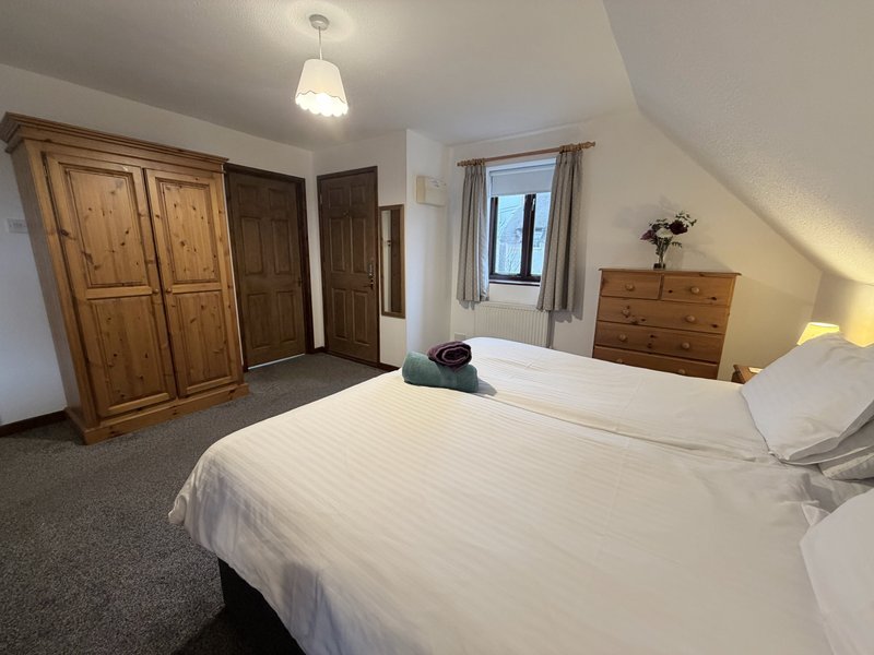 Spacious bedroom with double bed, wooden wardrobes, chest of drawers and window