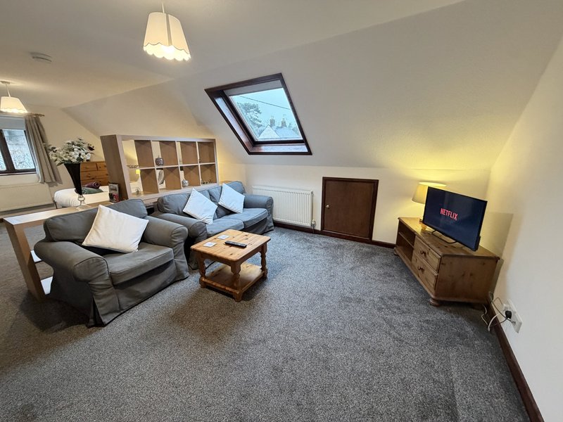 Attic living room with gray sofa, wooden coffee table, storage shelving and TV