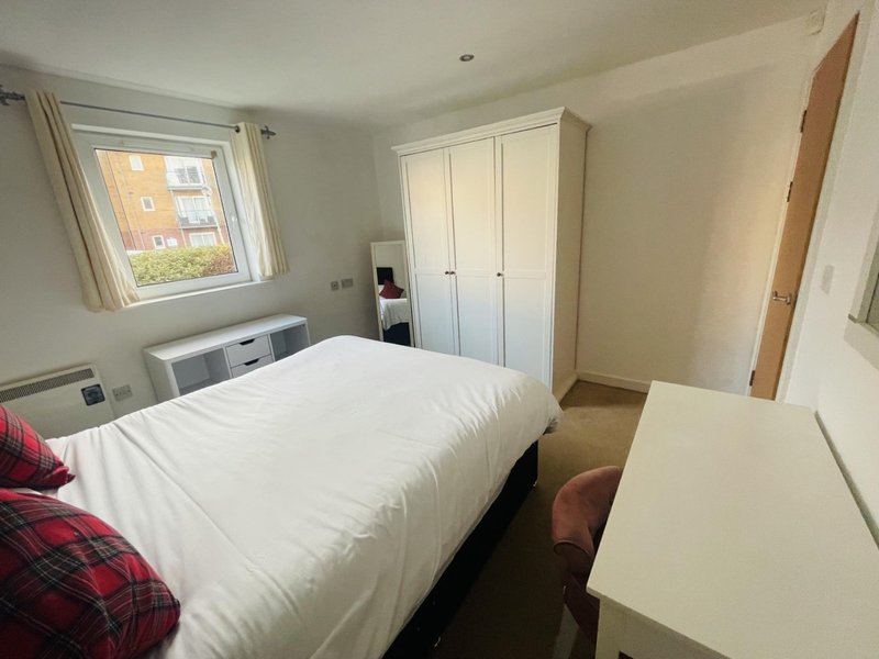 Bright bedroom with double bed, white wardrobe, desk, and window overlooking residential street