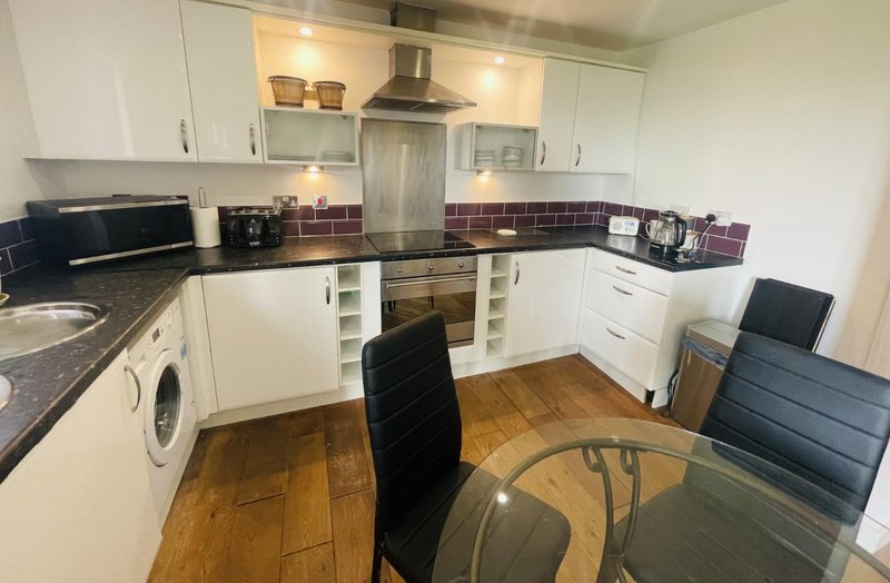 Modern kitchen with white cabinets, black countertops, burgundy tile splashback, and wooden flooring