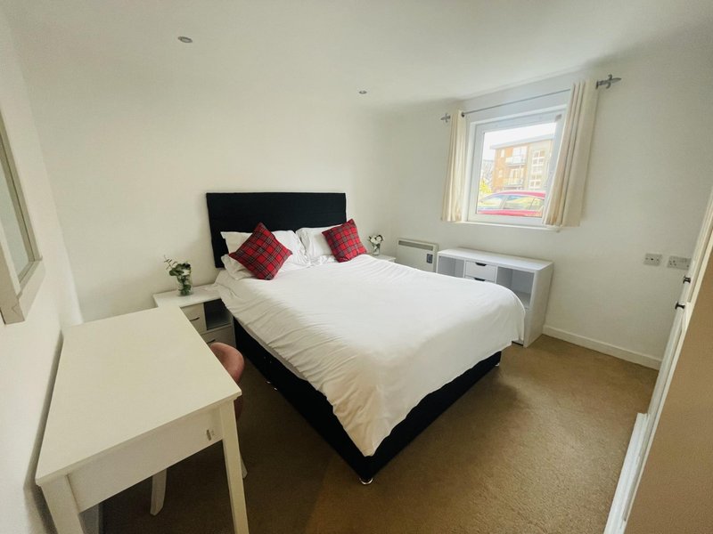 Bright bedroom with double bed, black headboard, red cushions, white desk and window