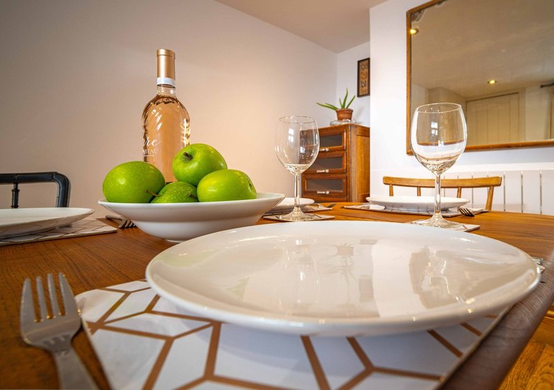 Dining table set with white plate, wine bottle, green apples, glasses and place settings