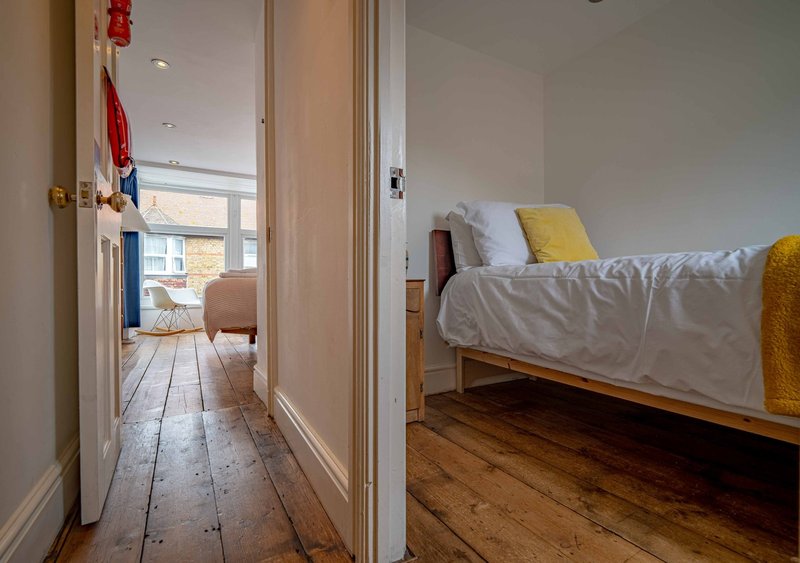 Bedroom with single bed, wooden floor, white walls and doorway to hallway