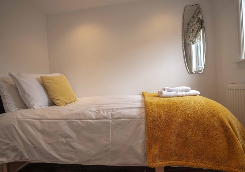 Bright bedroom with single bed, white bedding, yellow cushion and throw, oval mirror