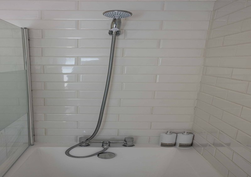 Bathroom shower area with white subway tile walls, overhead rainfall showerhead and chrome fixtures
