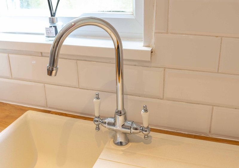 Modern kitchen sink with chrome mixer tap, cream subway tile splashback and window