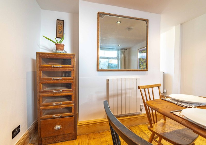 Bright room with wooden chest of drawers, mirror, radiator, and dining chairs
