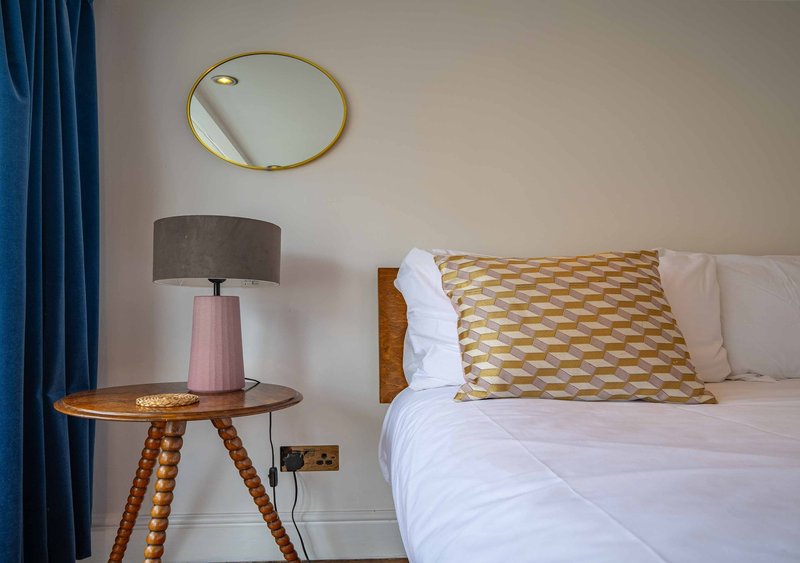 Bedroom with double bed, patterned cushion, tripod side table with lamp and mirror