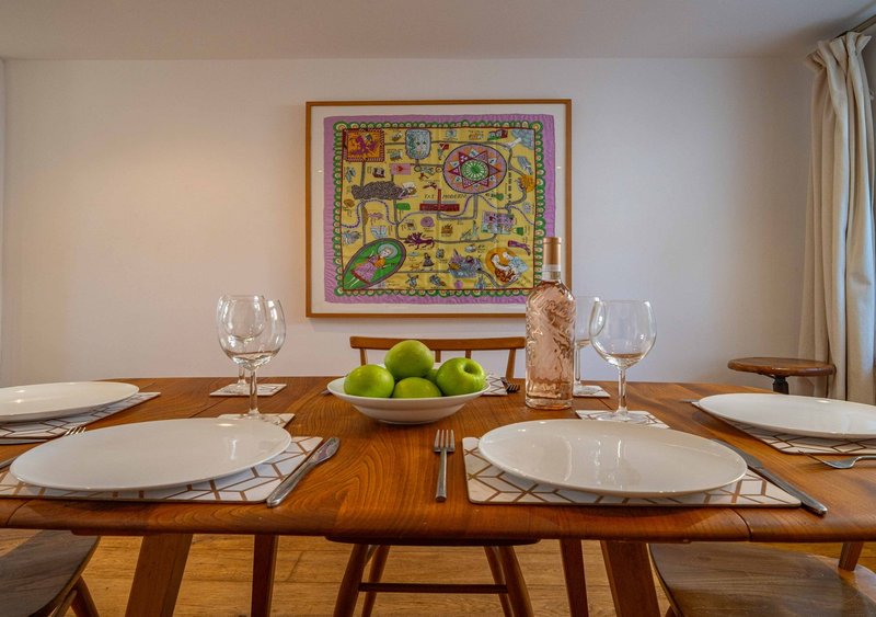Dining room with wooden table set for two, white plates, wine glasses, and fruit bowl