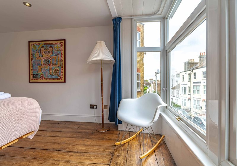 Bright bedroom with wooden floor, modern chair, floor lamp, and large windows overlooking urban street