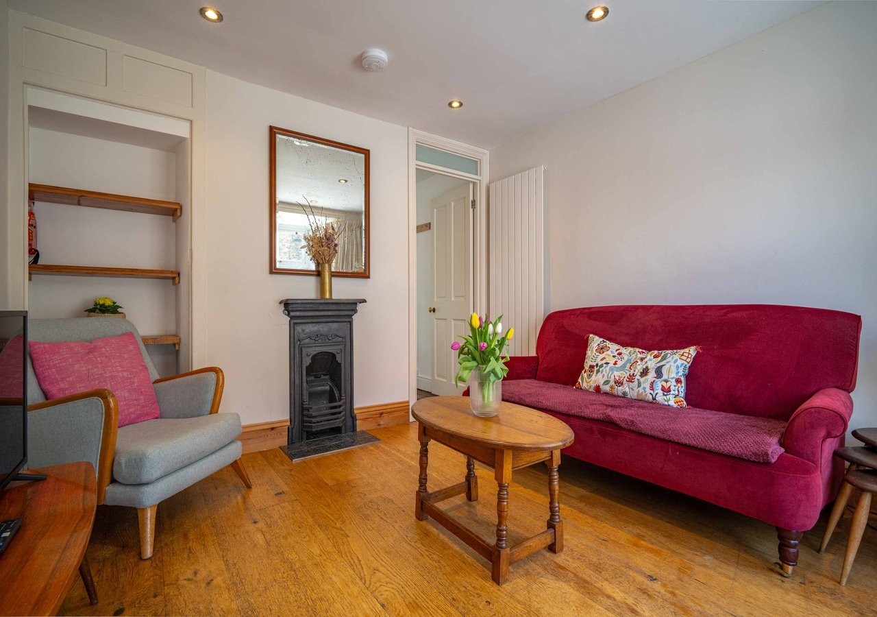 Bright living room with red sofa, grey armchair, fireplace, wooden floor and wall shelving