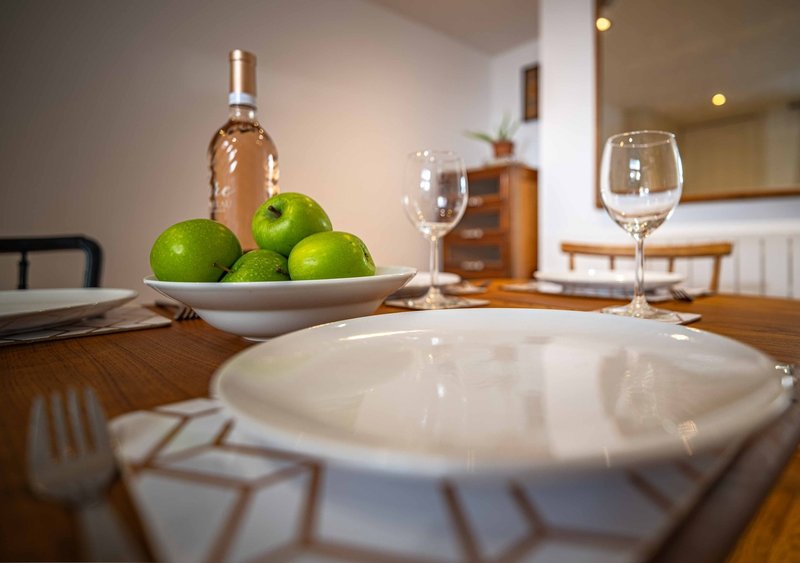Dining table set with place settings, green apples in bowl, wine bottle and glasses