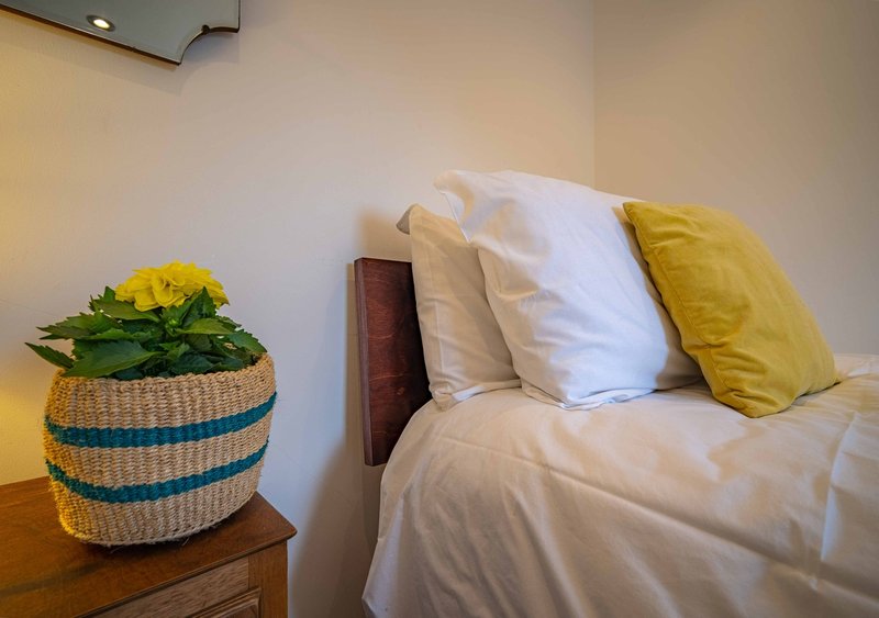 Bedroom with double bed, white and yellow pillows, potted yellow flowers on wooden nightstand