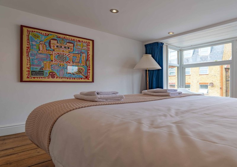 Bright bedroom with double bed, wooden floor, framed wall art and large windows