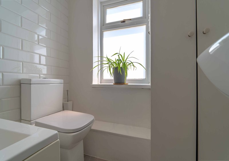 Clean bathroom with white subway tile walls, toilet, window with potted plant, and sink
