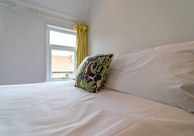 Bright bedroom with white bed, yellow curtains, and decorative cushion by window