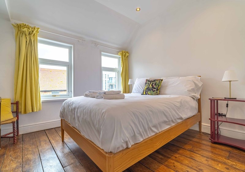 Bright bedroom with wooden bed, white bedding, yellow curtains and hardwood flooring