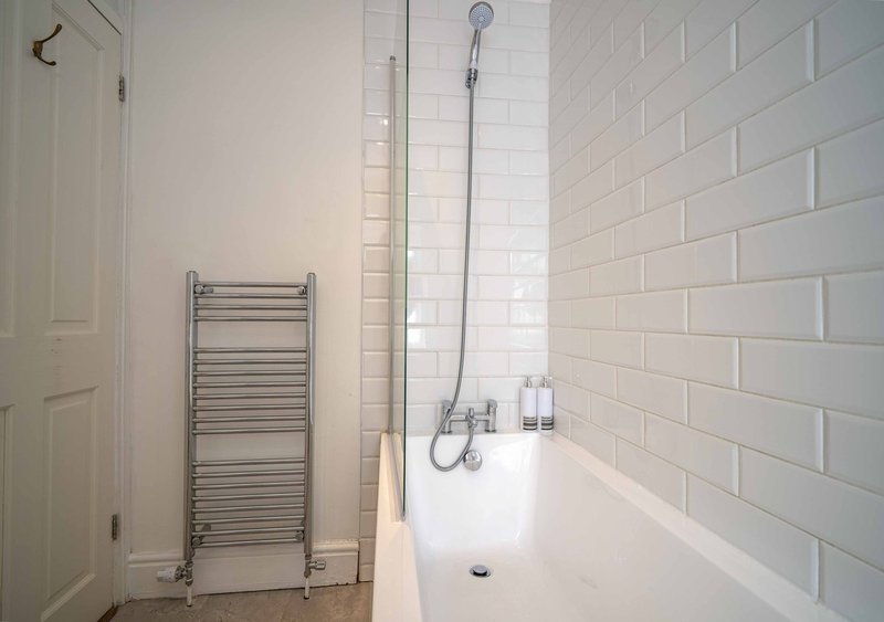 Bathroom with white subway tile walls, bathtub, towel rail and shower fixtures
