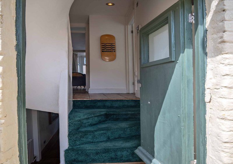 Narrow hallway with green carpet, white walls, wooden door frame and wall-mounted light fixture