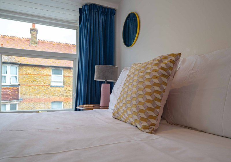 Bright bedroom with double bed, patterned cushion, blue curtains and window view