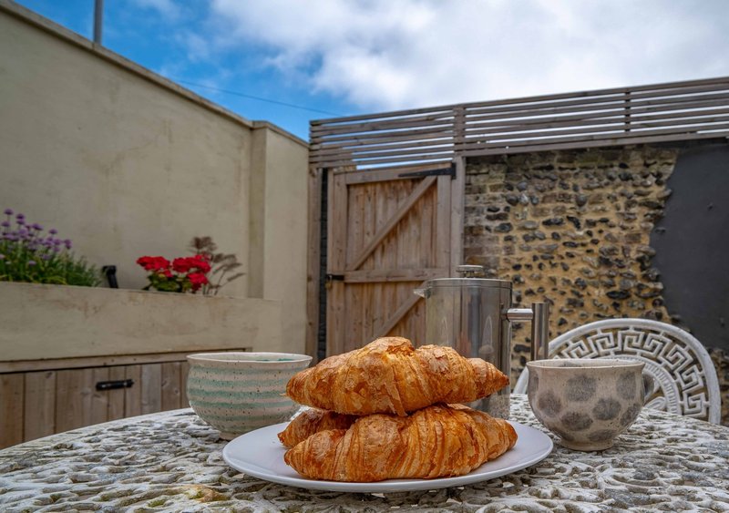 Outdoor patio table with croissants, flowers and stone wall backdrop