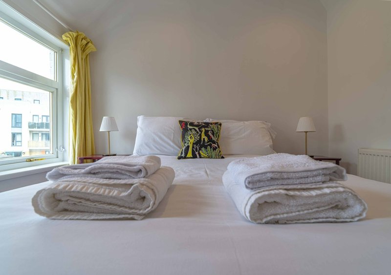 Bright bedroom with double bed, folded towels, yellow curtains and window view