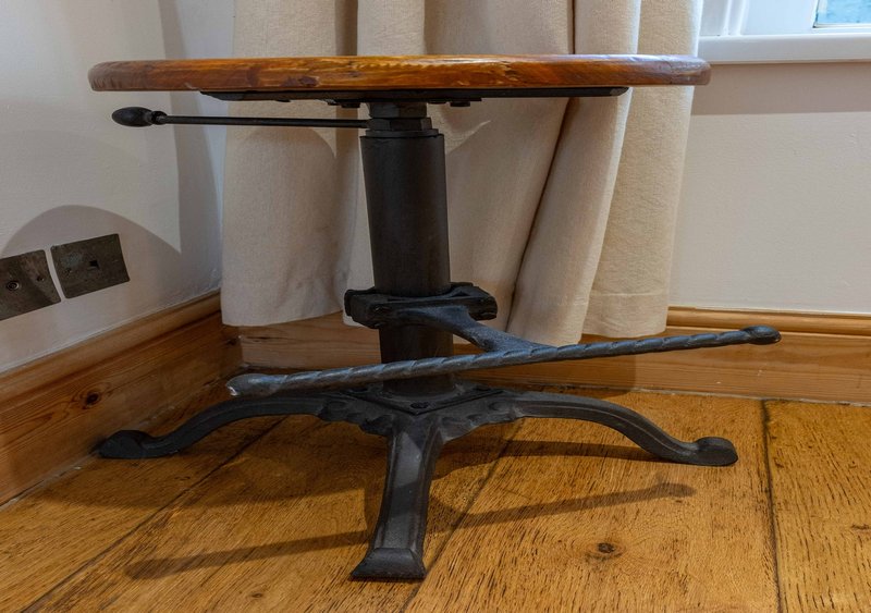 Wooden pedestal table with dark metal base on hardwood floor, cream curtains in background