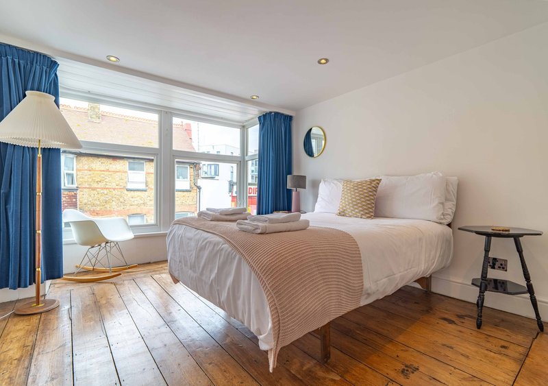 Modern bedroom with double bed, blue curtains, wooden floors and large windows