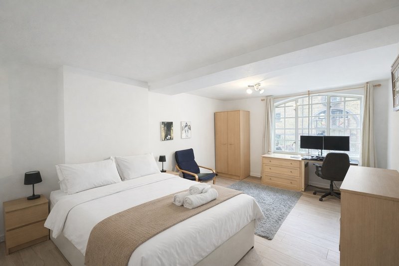 Bright bedroom with double bed, wooden furniture, desk area, and large windows