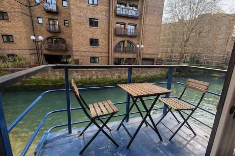 Outdoor terrace with wooden folding chairs and table overlooking canal and brick buildings