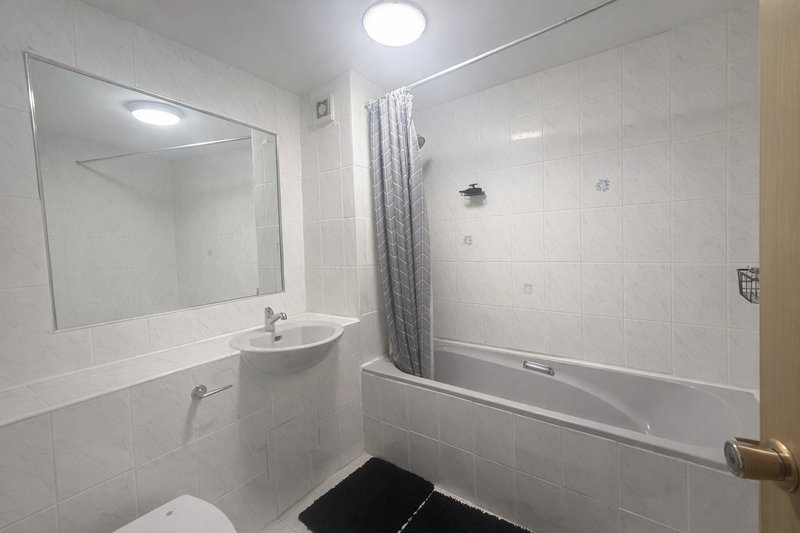 Clean white-tiled bathroom with sink, mirror, bathtub and shower curtain