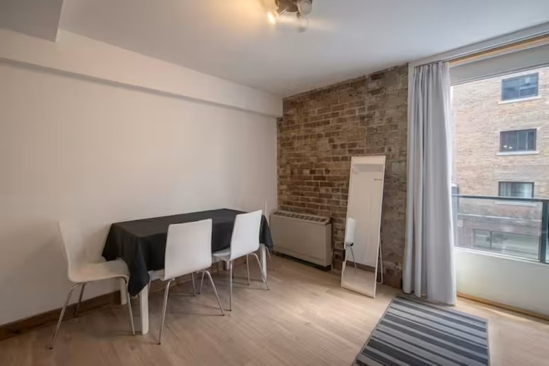 Open-plan dining and living area with exposed brick wall, dining table, chairs and balcony access