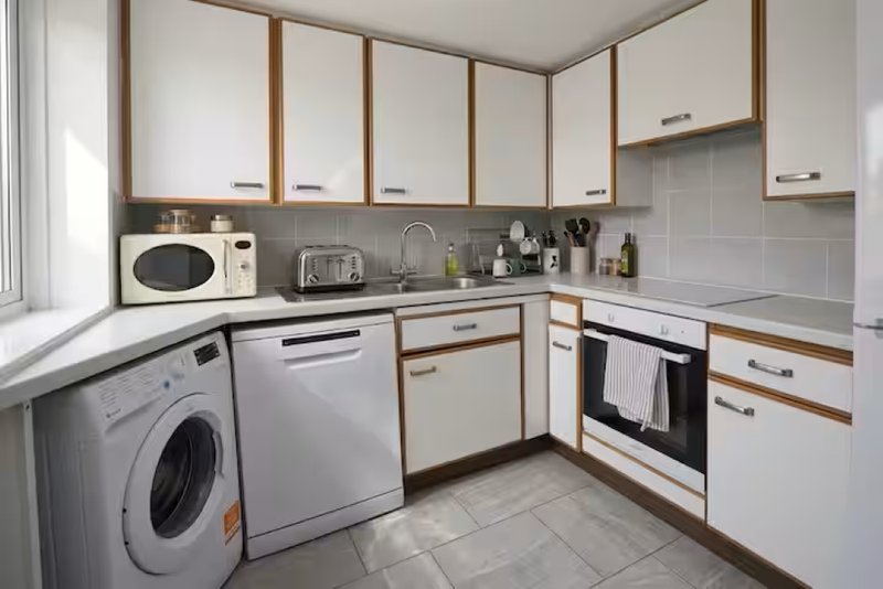 Modern kitchen with white cabinetry, integrated appliances, tiled floor and window