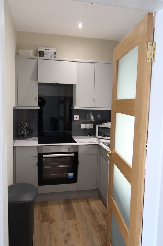 Modern compact kitchen with built-in oven, hob, white cabinetry and wooden flooring