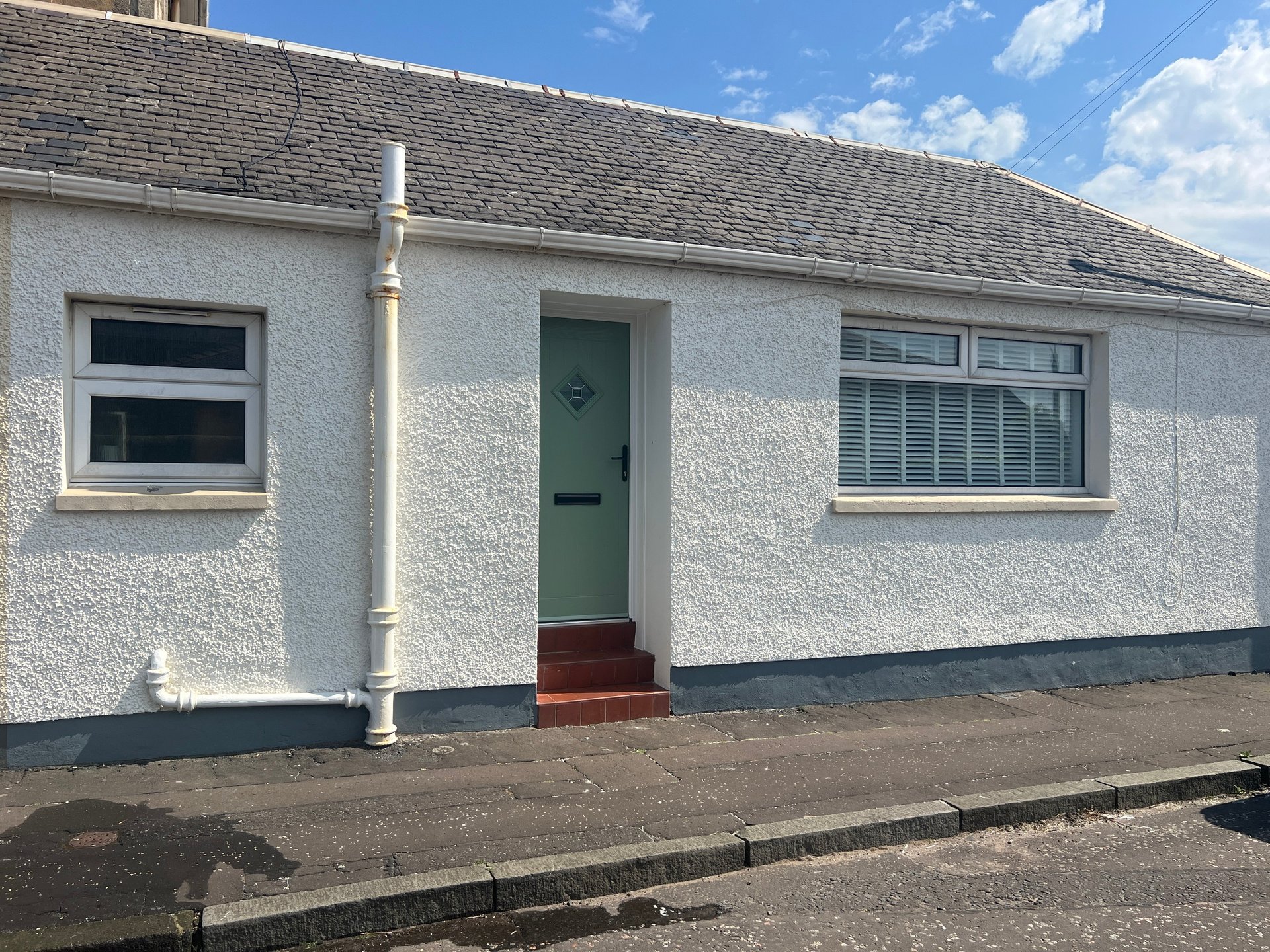 White rendered bungalow exterior with green door, two windows and slate roof