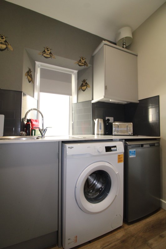 Compact kitchen with washing machine, black countertop, white cabinetry and window