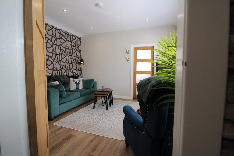 Modern living room with teal sofa, patterned wall hanging, potted plant and wooden flooring