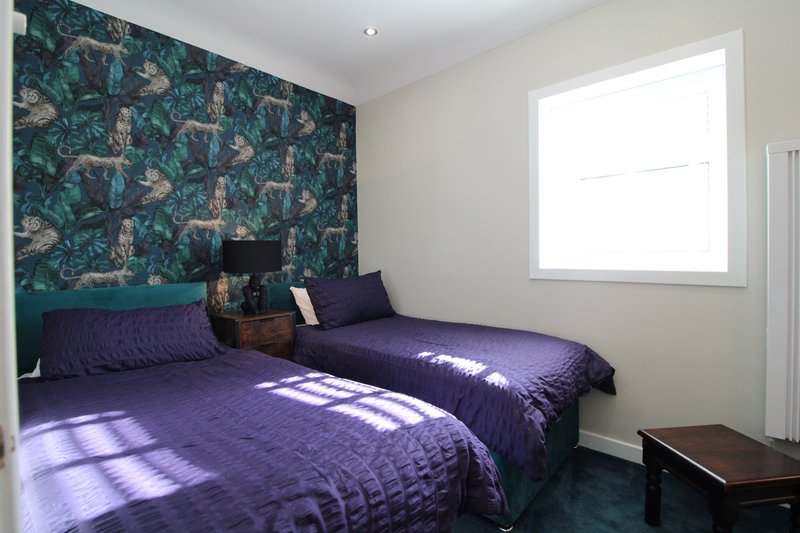 Bedroom with twin beds, purple bedding, patterned feature wall and bright window