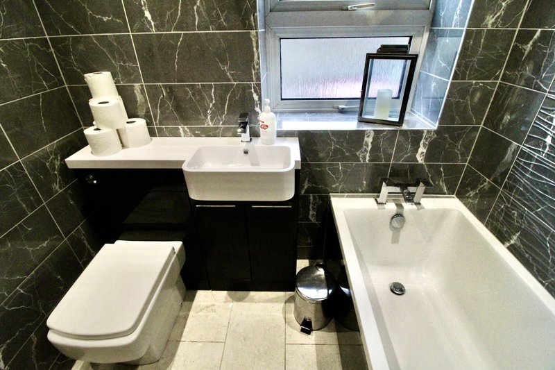 Modern bathroom with black and white tiles, white toilet, sink, bathtub and mirror