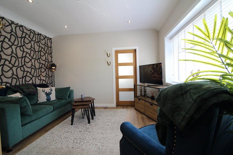 Bright living room with teal sofa, blue armchair, wooden TV stand, patterned wallpaper and potted plant