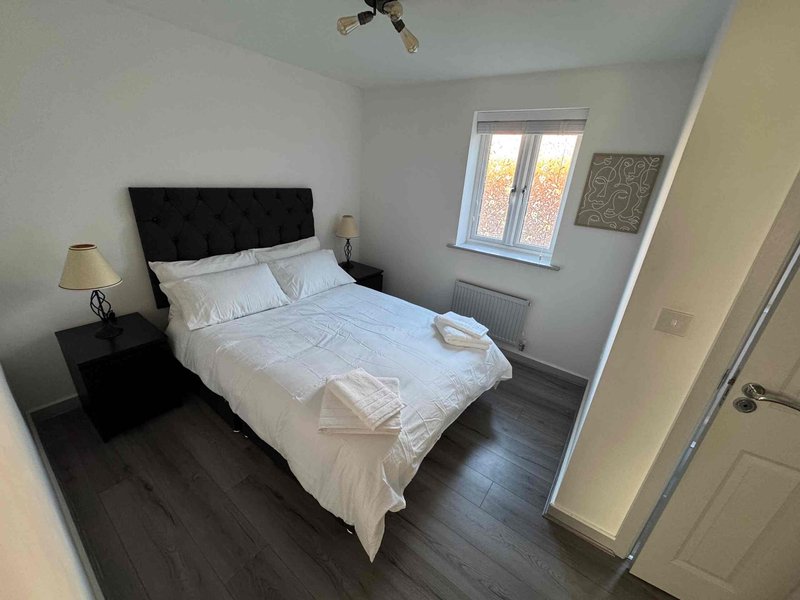 Bright bedroom with double bed, black headboard, wooden floor and window