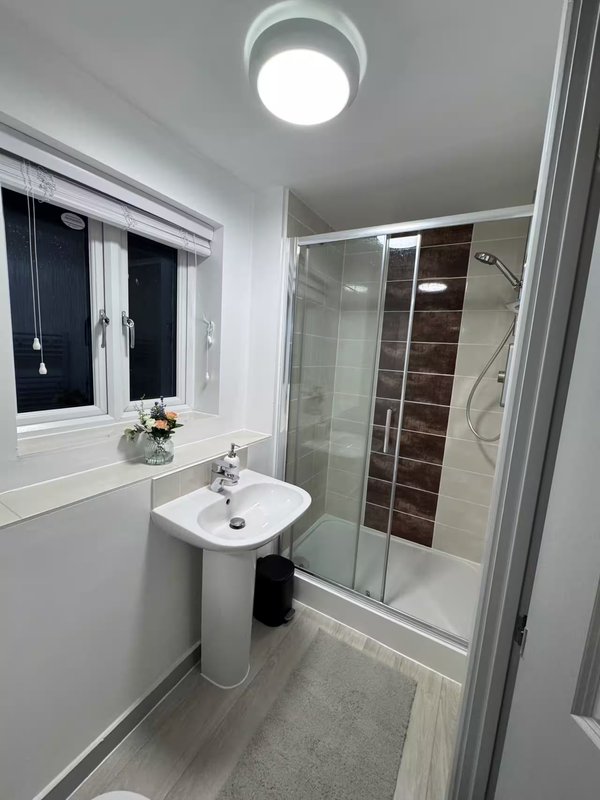 Modern bathroom with pedestal sink, shower enclosure, round ceiling light and window