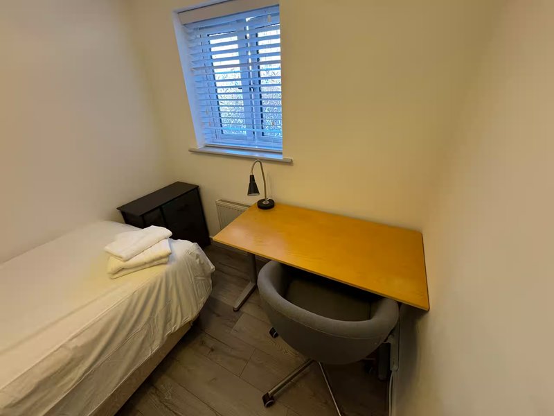 Small bedroom with single bed, wooden desk, office chair and window with shutters