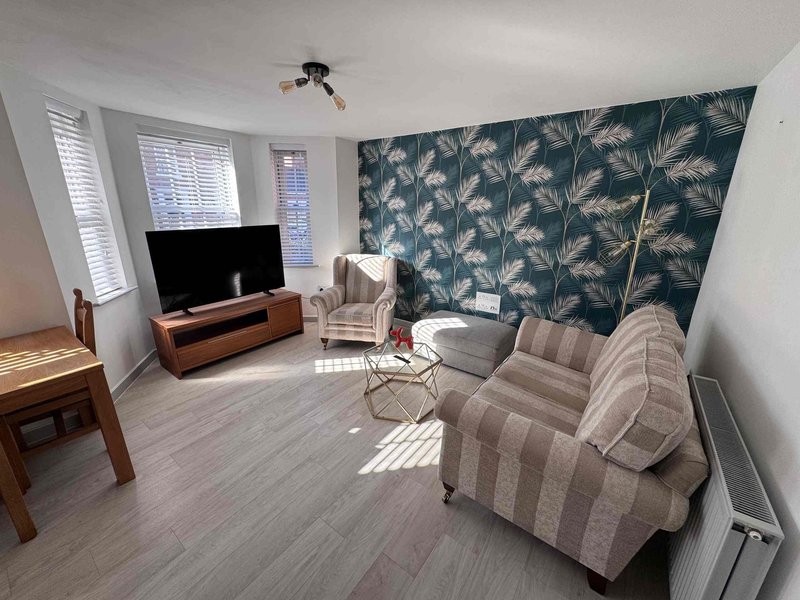 Bright living room with striped sofa, TV stand, armchair, patterned accent wall and windows