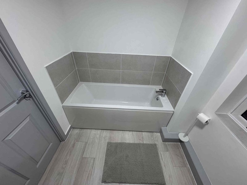 Modern bathroom with white bathtub, gray tile surround, and wood-effect flooring