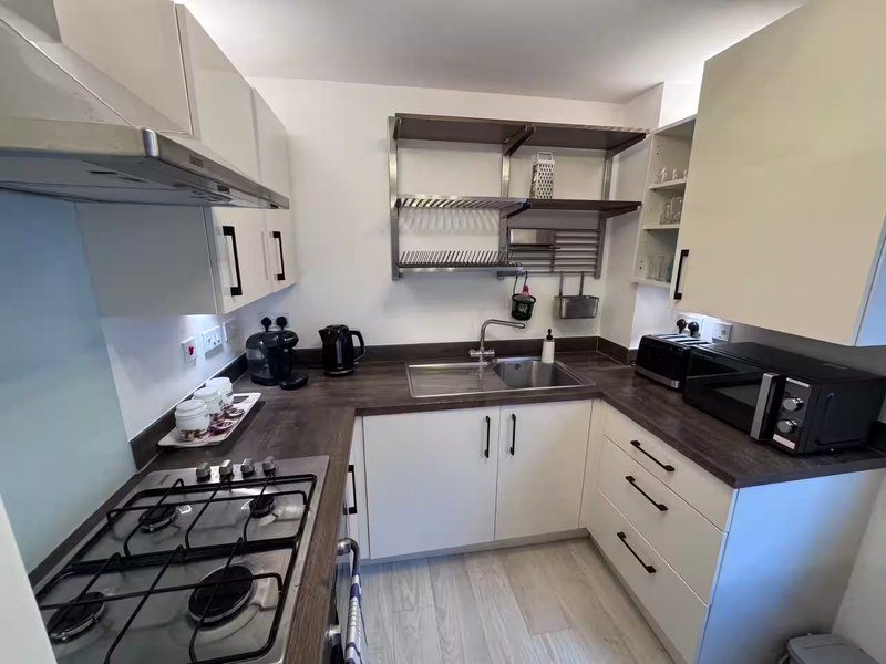 Modern kitchen with white units, dark worktops, gas hob, and wall-mounted shelving